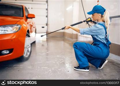 Female washer in uniform cleans wheel with high pressure gun in hands, car wash. Woman washes vehicle, carwash station, car-wash business