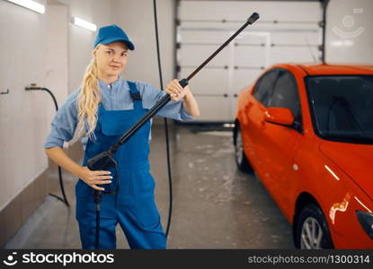 Female washer in uniform poses with high pressure gun in hands, car wash service. Woman cleans vehicle, carwash station, car-wash business