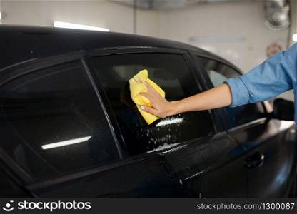 Female washer with sponge wipes the automobile glass, car wash. Woman cleans vehicle, carwash station, car-wash business