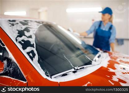 Female washer with sponge wipes the automobile windshield, car wash. Woman cleans vehicle, a carwash shop. Female washer wipes the automobile windshield