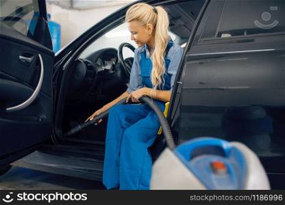Female washer with vacuum cleaner cleans auto interior, car wash service. Woman washes vehicle, carwash station, car-wash business