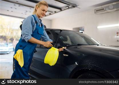 Female washer with wax spray cleans automobile, waxing on car wash service. Woman washes vehicle, carwash station, car wash business. Female washer with wax spray, car wash service