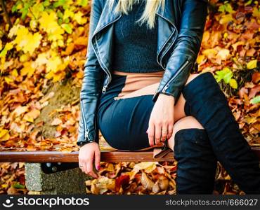 Female wearing sexy autumn outfit. Woman having short pink skirt, leather jacket and high knee black boots shoes, sitting on bench in park.. Woman wearing sexy autumn outfit