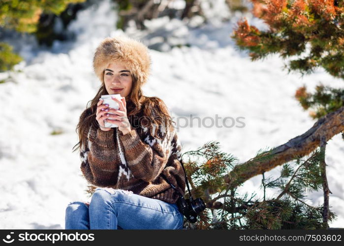 Female wearing winter clothes drinking hot coffee. Young woman enjoying the snowy mountains in winter, in Sierra Nevada, Granada, Spain.. Young woman enjoying the snowy mountains in winter