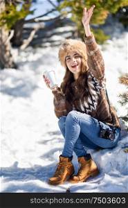 Female wearing winter clothes drinking hot coffee. Young woman enjoying the snowy mountains in winter, in Sierra Nevada, Granada, Spain.. Young woman enjoying the snowy mountains in winter
