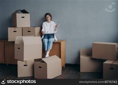 Female with laptop sitting surrounded by cardboard boxes with personal stuff. Woman searching moving company, selects mover for relocation. Transportation services concept, copy space.. Female with carton boxes searching moving company at laptop for relocation. Transportation service