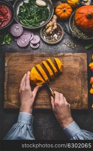 Female woman hands cut pumpkin on cutting board with knife and various vegetables and seasoning ingredients for tasty seasonal dish cooking, rustic , top view. Healthy and clean eating