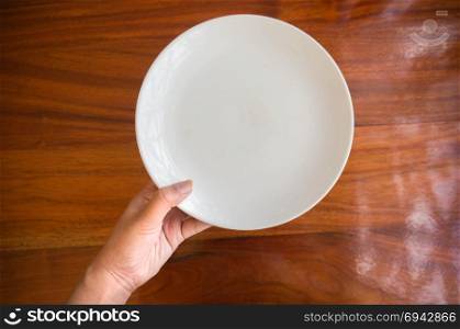Female (woman) hands hold (support) a white dish (plate) on wooden table