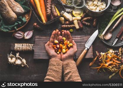 Female woman hands holding diced colorful vegetables on rustic kitchen table with vegetarian cooking ingredients and tools. Healthy and clean food cooking and eating concept.