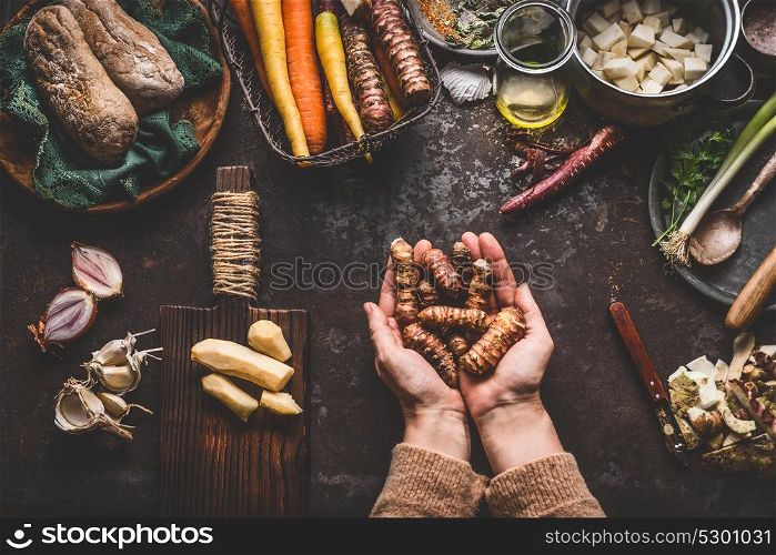 Female woman hands holding jerusalem artichokes or earth pear vegetables on rustic kitchen table with vegetarian cooking ingredients and tools. Healthy and clean food cooking and eating concept.