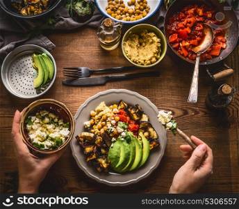 Female woman hands served healthy vegetarian meal in bowl with chick peas puree, roasted vegetables , red paprika tomatoes stew, avocado and seeds . Clean eating, dieting, vegetarian food concept