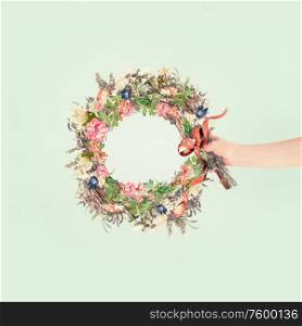 Female women hand holding summer flowers wreath with ribbon at light mint background. Creative flowers arrangement concept