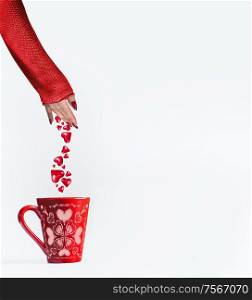 Female women hand in red pullover sprinkles hearts in mug on white background. Declaration of love and Valentines day concept