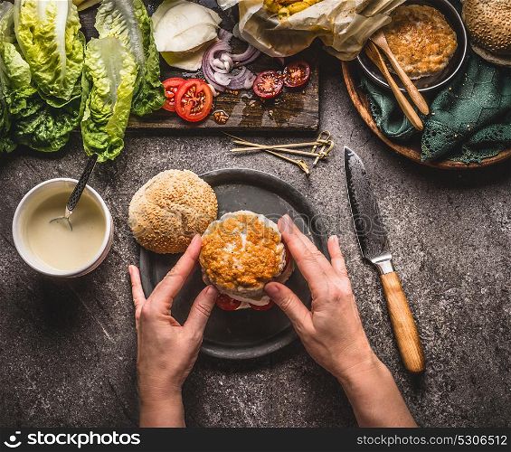Female women hands making homemade tasty burger with chicken on rustic kitchen table background with ingredients, top view
