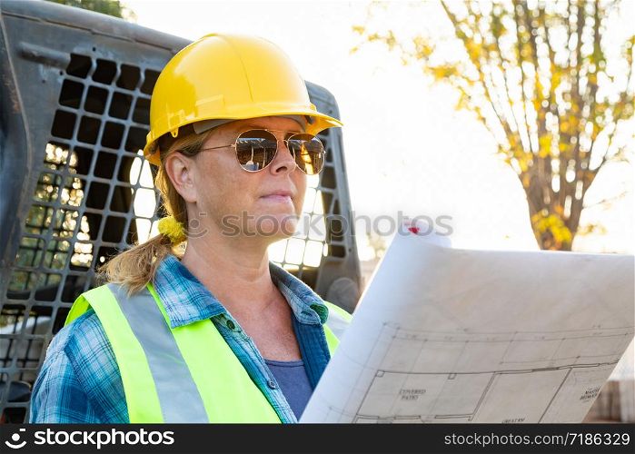 Female Worker Holding Technical Blueprints Near Small Bulldozer At Construction Site