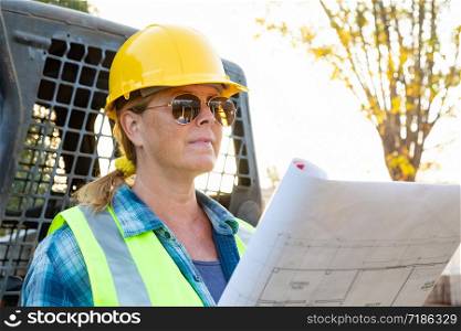 Female Worker Holding Technical Blueprints Near Small Bulldozer At Construction Site