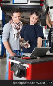 Female worker using laptop while standing next to client in garage with person in the background