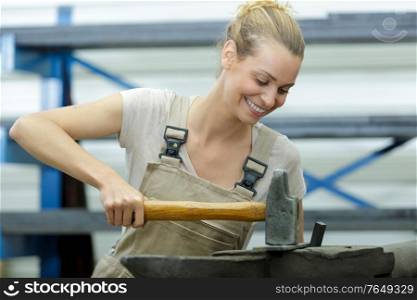 female workers shaping metal with hammer over anvil