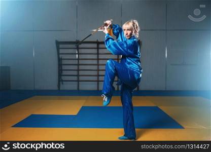 Female wushu fighter with sword in action, martial arts. Woman in blue cloth poses with blade. Female wushu fighter with sword in action
