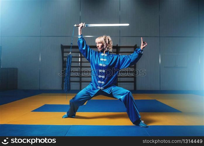 Female wushu fighter with sword in action, martial arts. Woman in blue cloth poses with blade. Female wushu fighter with sword in action