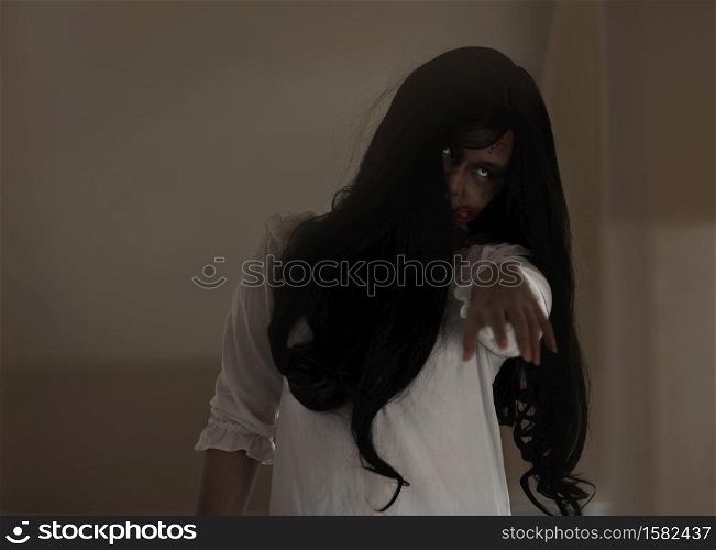 Female zombie in blood. Asian Woman ghost with blood. Horror scary fear in house dark tone raise hand and reach out. Closeup hair covering the face her eye looking camera, Halloween festival concept