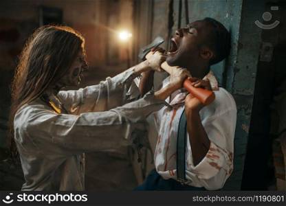Female zombie with axe attacked a man in abandoned factory, scary place. Horror in city, creepy crawlies, doomsday apocalypse, bloody evil monsters