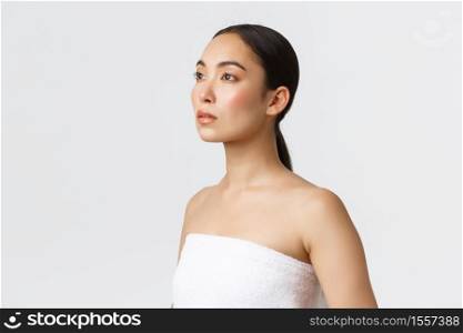 Feminine beautiful asian woman in white towel looking left dreamy. Girl with clean perfect skin, advertising skincare products, bathroom cosmetics, standing white background.. Feminine beautiful asian woman in white towel looking left dreamy. Girl with clean perfect skin, advertising skincare products, bathroom cosmetics, standing white background