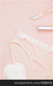 Feminine flat lay set of female panties and accessories, perfumes, lipstick and pads liners on pastel pink color background for fashion blog and social media with copy space for text