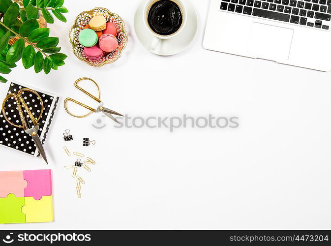 Feminine office desk workplace. Coffee, cookies, laptop computer and gren plant on white table background. Top view. Flat lay