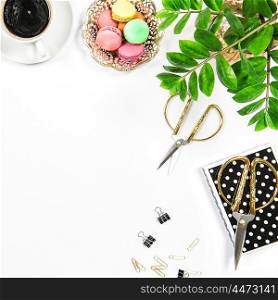 Feminine workplace with coffee, macarons cookies, office supplies and green plant on white table background. Flat lay