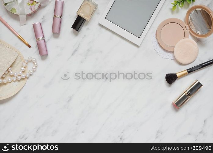 Feminine workspace on table desk with smartphone, lipstick, pearl necklace, compact powder, cosmetic brushes and nail polish on marble stone background; top view, flat lay