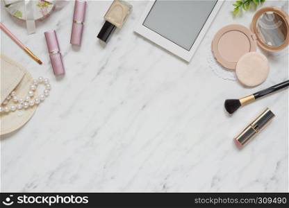 Feminine workspace on table desk with smartphone, lipstick, pearl necklace, compact powder, cosmetic brushes and nail polish on marble stone background; top view, flat lay