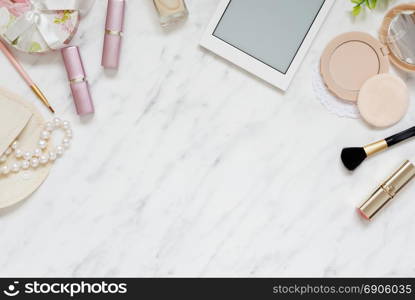 Feminine workspace on table desk with smartphone, lipstick; pearl necklace, compact powder, cosmetic brushes and nail polish on marble stone background; top view, flat lay