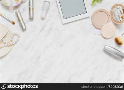 Feminine workspace on table desk with smartphone, lipstick; pearl necklace, compact powder and cosmetic brushes are on marble stone background; top view, flat lay