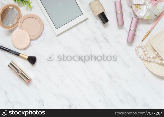 Feminine workspace on table desk with smartphone, lipstick; pearl necklace, compact powder, cosmetic brushes and nail polish on marble stone background; top view, flat lay