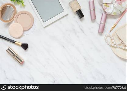 Feminine workspace on table desk with smartphone, lipstick; pearl necklace, compact powder, cosmetic brushes and nail polish on marble stone background; top view, flat lay