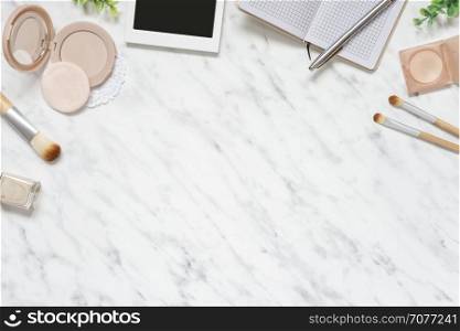 Feminine workspace on table desk with smartphone, notebook, pen, compact powder, cosmetic brushes and nail polish on marble stone background; top view, flat lay