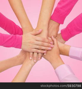 feminism, women power and breast cancer awareness concept - close up of women hands on top of each other over white background