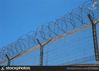 Fence with spiral barbed wire on top on sky background