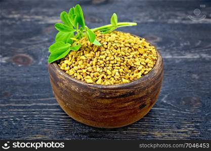Fenugreek in a clay bowl with green leaves on a wooden plank background