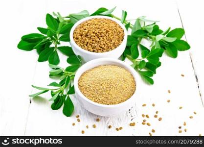Fenugreek seeds and ground spice in two bowls and on a table with green leaves on white wooden board background