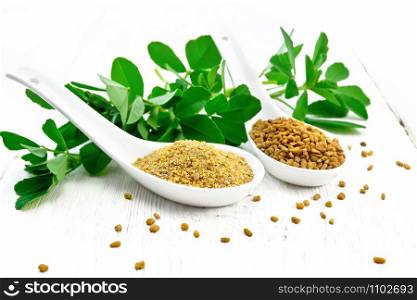 Fenugreek seeds and ground spice in two spoons and on a table with green leaves on background of light wooden board