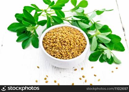 Fenugreek seeds in a bowl and on a table, seasoning leaves on wooden board background