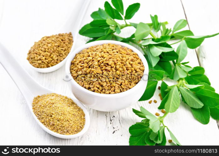 Fenugreek seeds in a bowl and spoon, ground spice in a spoon with green leaves on a background of light wooden board