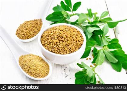 Fenugreek seeds in a bowl and spoon, ground spice in a spoon with green leaves on a background of light wooden board