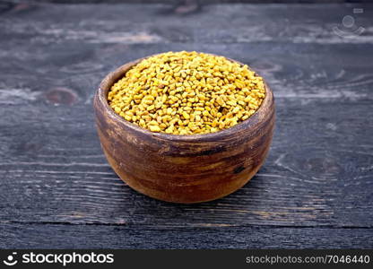 Fenugreek seeds in a clay bowl on the background of a black wooden board