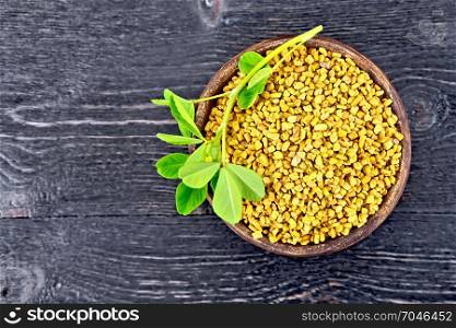 Fenugreek seeds in a clay bowl with green leaves on a wooden plank background. Fenugreek with leaf in clay bowl on board top