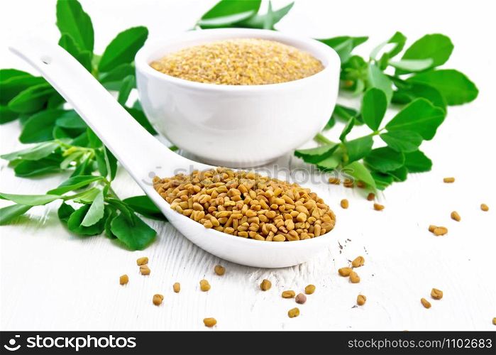 Fenugreek seeds in a spoon and ground spice in a bowl with green leaves on background of light wooden board