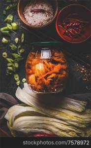 Fermented chinese cabbage marinated in hot chili sauce, kimchi, in glas jar on rustic background with ingredients. Top view