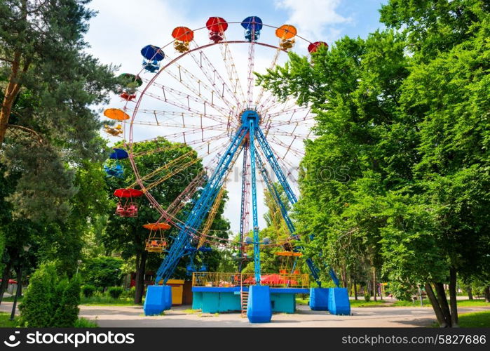 Ferris wheel in the green park over blue sky with clouds